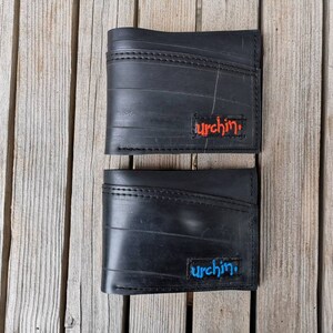 Puede incluir: Dos carteras de cuero negro con la palabra "urchin" cosida en naranja y azul en la parte delantera.