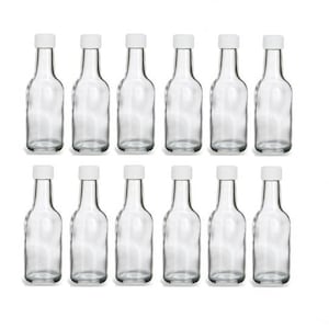 Puede incluir: Conjunto de doce botellas de vidrio transparente con tapas de plástico blanco. Las botellas son pequeñas y estrechas, con un fondo redondeado y una parte superior ligeramente acampanada.