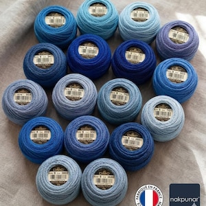 May include: An assortment of DMC cotton perle thread balls in various shades of blue, from light to dark. Each ball has a label with the DMC logo and a product code. The image includes a French flag and the nakpunar logo.