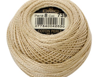 Puede incluir: Una madeja beige de hilo de bordar de algodón DMC Perle 8, etiquetada con el número 739 y un código de barras. La etiqueta también dice "Coton Perle 10g."