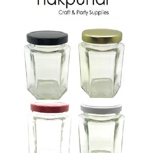 May include: Four glass jars with hexagonal sides and different colored lids. The lids are black, gold, red, and white. The jars are empty and appear to be for crafts or party supplies.