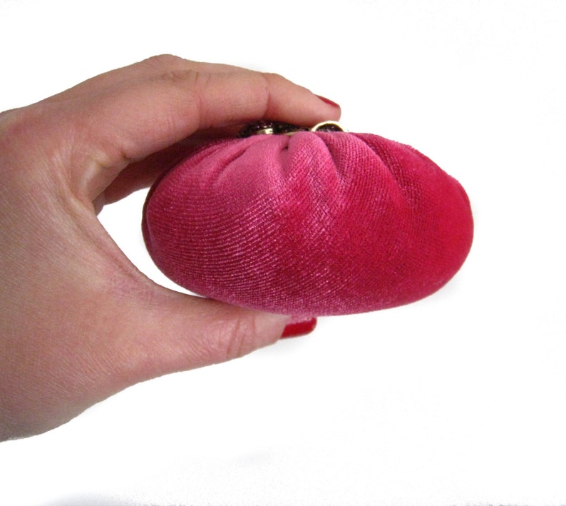 May include: A small, round, pink velvet pouch with a gold clasp.