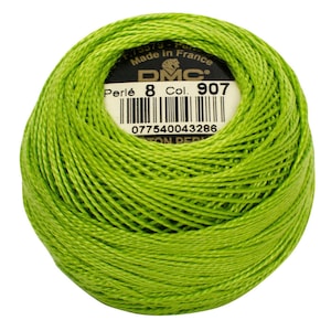 May include: A ball of bright green DMC Perlé cotton thread, Col. 907, for embroidery or needlework. The label indicates it's made in France. The thread is tightly wound, showing the texture of the cotton. The barcode and other details are visible on the label.