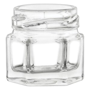 Puede incluir: Un tarro de vidrio transparente con forma hexagonal y tapa de rosca. El tarro está vacío y tiene una superficie lisa y pulida.