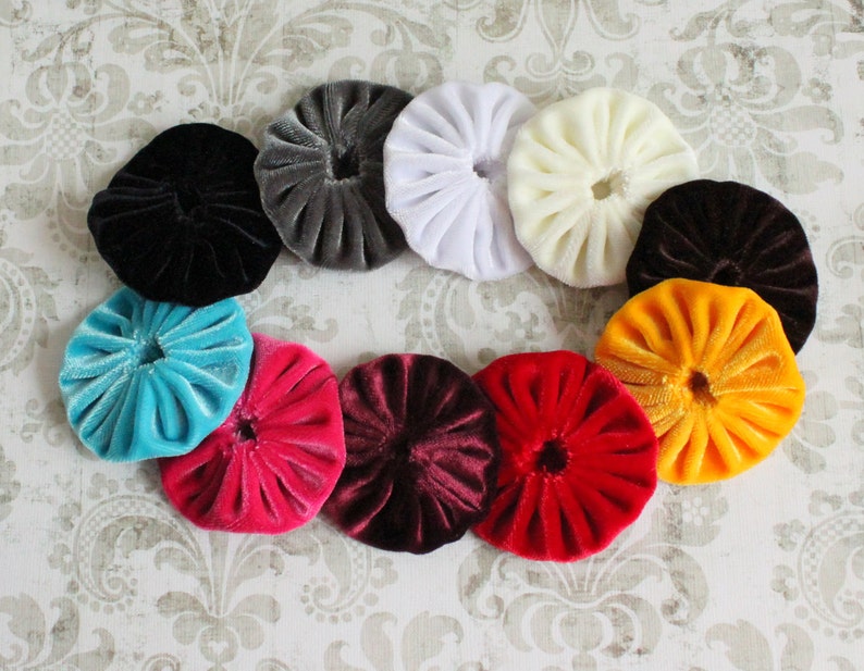 May include: Assortment of 10 round fabric covered buttons in various colors, including black, gray, white, turquoise, pink, maroon, red, yellow, and orange. The buttons are all the same size and have a ruffled texture.