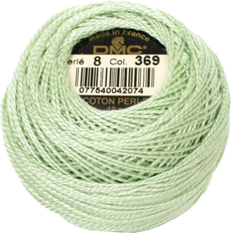 May include: A ball of light green DMC Perle cotton thread, color 369, with a label indicating it's made in France. The thread is tightly wound, showing the texture of the cotton. Ideal for embroidery and needlework projects.