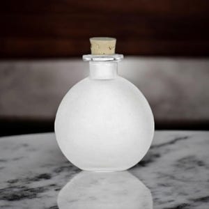 Puede incluir: Una botella de vidrio esmerilado con un tapón de corcho. La botella es redonda y tiene un acabado esmerilado liso.