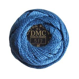 May include: A ball of blue DMC embroidery floss. The label reads "COTON PERLE 10 g DMC MADE IN FRANCE 5.17". The thread is tightly wound, showing a gradient of blue shades. Ideal for embroidery and needlework projects.