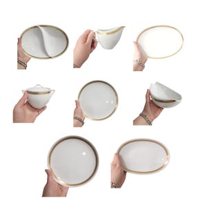 May include: A collection of white porcelain serving dishes with gold trim. The set includes oval platters, a creamer, a sugar bowl with a lid, and a round plate. The dishes are held by hands against a white background.