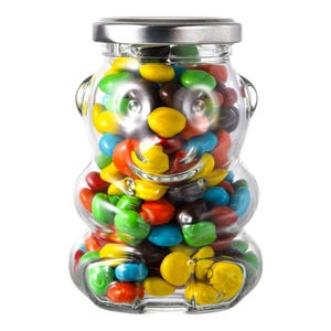 May include: A clear glass jar shaped like a bear filled with colorful candy. The candy is a mix of yellow, red, green, blue, brown, and orange.
