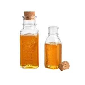 May include: Two glass honey jars with cork lids. The larger jar is labeled "One Pound Pure Honey".