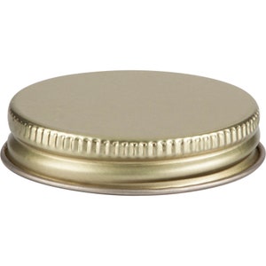 Puede incluir: Tapa de metal dorado con parte superior lisa y borde acanalado.