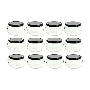 May include: Twelve clear glass jars with black lids are arranged in a grid. The jars have a rounded shape with a wide opening and a slightly curved body. The black lids provide a contrast to the transparent glass.