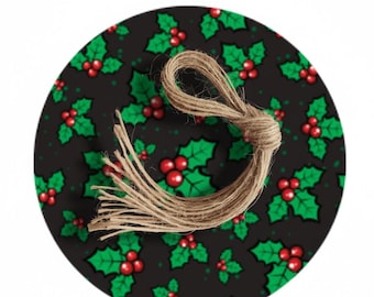 May include: A round Christmas ornament with a black background featuring a pattern of green holly leaves and red berries. A natural twine loop is attached at the top. Festive holiday decor.