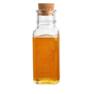 May include: A clear glass bottle with a cork stopper filled with honey. The bottle has an embossed design of a honeycomb and the text "ONE POUND PURE HONEY".
