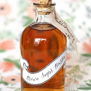 Puede incluir: Una botella de vidrio transparente llena de un l&iacute;quido marr&oacute;n, sellada con un tap&oacute;n de corcho. Una etiqueta blanca con las palabras "Brown Sugar Bourbon" envuelve la botella. Una etiqueta con "Katie Foundry No. 3" est&aacute; atada a la botella.