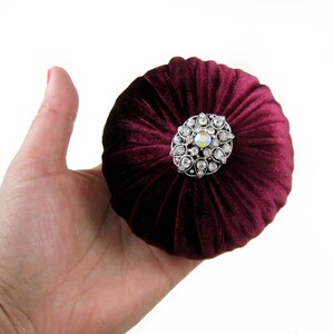 May include: A burgundy velvet pincushion with a decorative silver and crystal brooch.