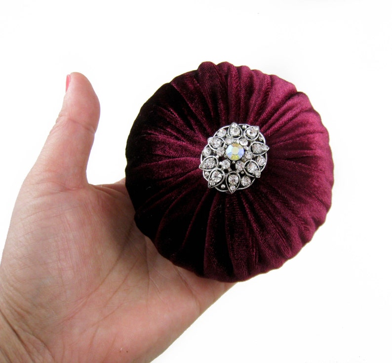 May include: A burgundy velvet pincushion with a decorative silver and crystal brooch.