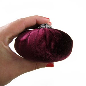May include: A small, round, burgundy velvet pincushion with a silver and rhinestone embellishment on top.