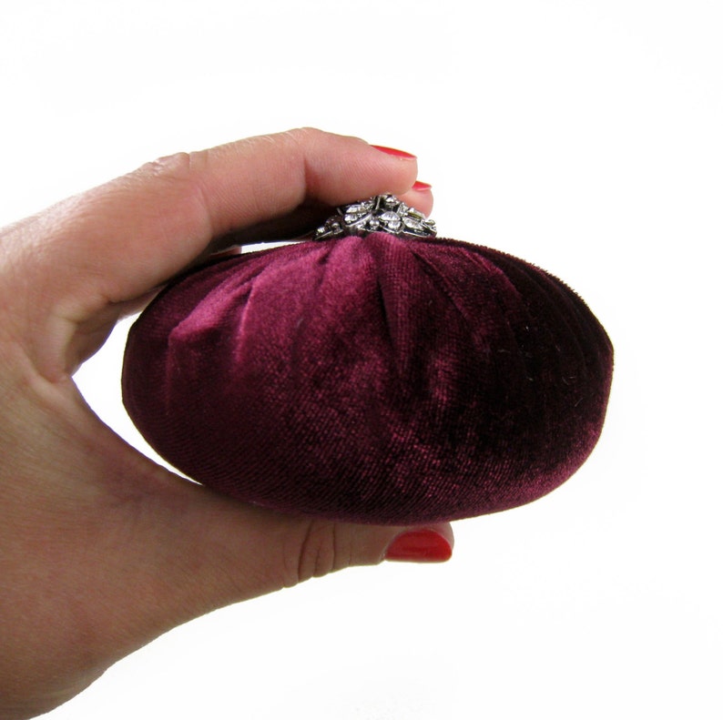 May include: A small, round, burgundy velvet pincushion with a silver and rhinestone embellishment on top.