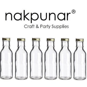 May include: Six clear glass bottles with gold-coloured lids are displayed in a row. The bottles are empty and have a classic shape. The text "nakpunar Craft & Party Supplies" is printed above the bottles.