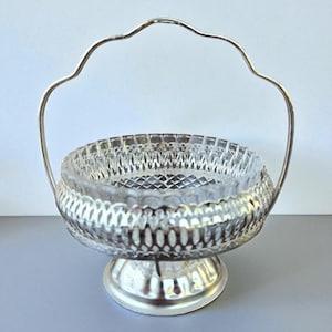 Puede incluir: Cesta de servir plateada con un cuenco de cristal transparente. El cuenco presenta un patrón tallado en forma de diamante y se encuentra dentro de un marco plateado decorativo. Un asa curvada se arquea sobre el cuenco. Ideal para servir caramelos o pequeños dulces.