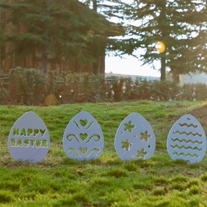 May include: Four white wooden Easter eggs with different designs. The first egg says "Happy Easter" on it. The second egg has a heart and wavy line design. The third egg has a flower design. The fourth egg has a wavy line design.
