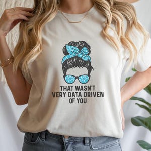 May include: White t-shirt featuring a graphic of a woman with a messy bun and sunglasses. The text "That wasn't very data driven of you" is printed below the graphic.