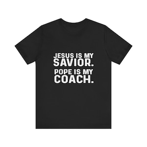 May include: Black t-shirt with white text that reads "JESUS IS MY SAVIOR. POPE IS MY COACH."