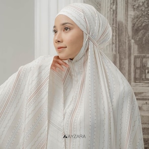 May include: A white headscarf and matching garment with vertical stripes in light brown and blue. The fabric has a delicate floral pattern. The brand name "AYZARA" is printed in black at the bottom.