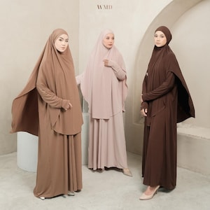 Puede incluir: Tres mujeres con vestidos modestos de manga larga y velos en tonos marrón y rosa. Los vestidos tienen un diseño fluido. Las letras "WMD" son visibles en la esquina superior derecha de la imagen.