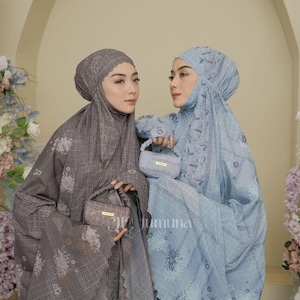 May include: Two individuals wearing matching prayer garments, one in dark gray and one in light blue, both featuring intricate floral patterns and lace-trimmed hoods. Each person holds a small, rectangular matching handbag with a gold-tone label.
