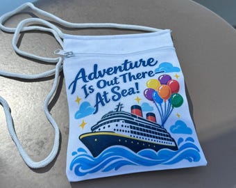 May include: A white crossbody bag with a zipper closure and white cord strap. The front features a graphic of a cruise ship on blue waves, a cluster of colorful balloons, and the text "Adventure Is Out There At Sea!" in blue script.