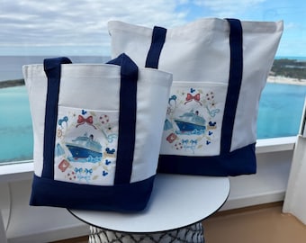 May include: Two white canvas tote bags with navy blue bottoms and handles. Each bag features a front pocket with a printed graphic of a cruise ship surrounded by nautical icons, red bows, and small blue mouse ear silhouettes.