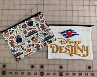 May include: Two zippered pouches. One features a white background with a pattern of Mickey Mouse, cruise ships, and the text "Castaway Cay." The other is white with the Disney Cruise Line logo and "Disney Destiny" in gold.