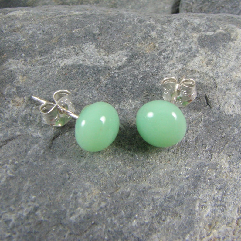 May include: A pair of silver stud earrings with light green round gemstones.