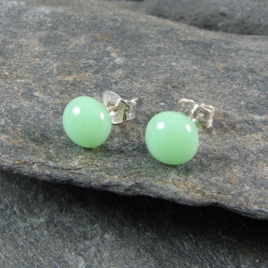 May include: A pair of silver stud earrings with round, light green gemstones.