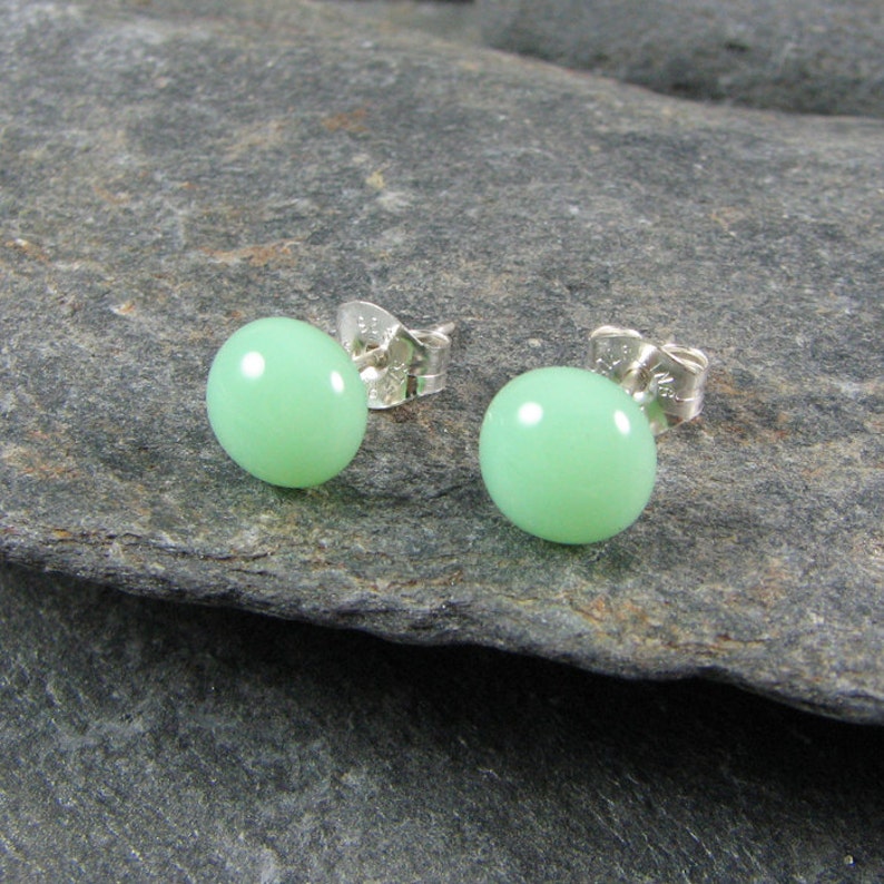 May include: A pair of silver stud earrings with round, light green gemstones.