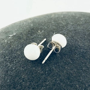 May include: A pair of white pearl stud earrings with silver posts and backs.