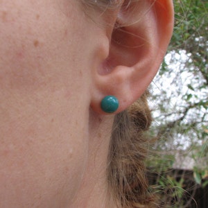 May include: A close-up of a person's ear with a teal blue stud earring. The earring is a simple round shape.