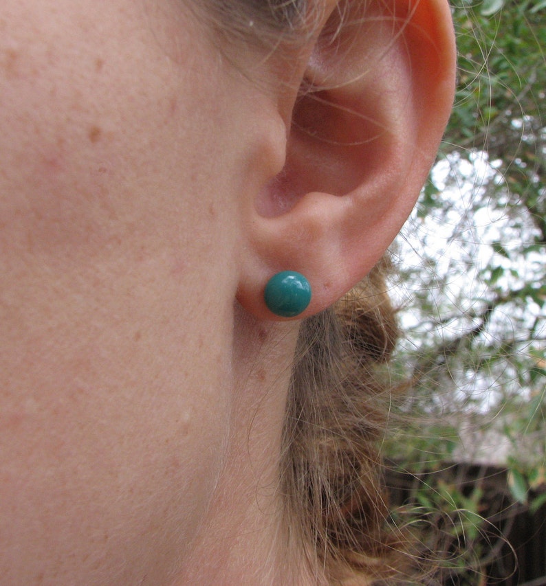 May include: A close-up of a person's ear with a teal blue stud earring. The earring is a simple round shape.