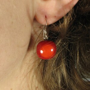 May include: A pair of silver earrings with a single red bead on each earring.