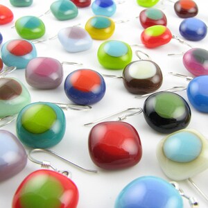 May include: Assortment of colorful glass earrings with various patterns and designs. Each earring features a round or square shaped glass piece with a contrasting colored circle or square in the center. The earrings are suspended from silver hooks.