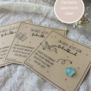 Könnte beinhalten: Eine Ansammlung von Karten aus Kraftpapier mit handgeschriebenem Text und Illustrationen, darunter ein Schmetterling und ein Vogel. Ein kleines, blaues sternförmiges Objekt ist ebenfalls vorhanden. Die Karten sind auf einem strukturierten, cremefarbenen Stoff angeordnet.