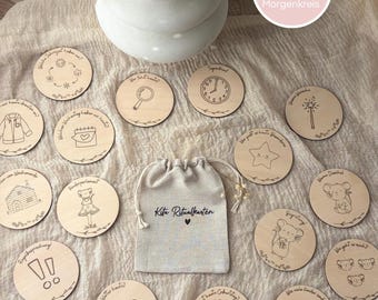May include: Wooden circle cards with etched illustrations and text, including a clock, star, and a house. A drawstring bag with "Kita Ritualkarten" is in the center. The cards are arranged on a beige surface.