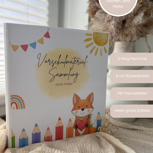 Könnte beinhalten: Ein weißer Ordner mit 2-Ring-Mechanik und 8 cm Rückenbreite, verziert mit einer Illustration eines Fuchses mit Herz, einer gelben Sonne, einem Regenbogen und Buntstiften. Der Text lautet Vorschulmaterial-Sammlung Jana Huber und enthält über 140 Vorlagen, Trennstreifen und gratis Dateien.