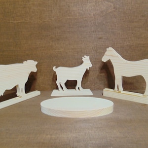 May include: Three wooden animal silhouettes on stands. A cow, a goat, and a horse are all made of unfinished wood.