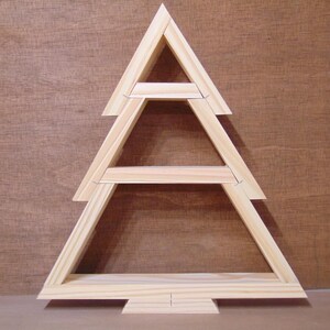 May include: A wooden Christmas tree-shaped shelf with three tiers. The tree is constructed from light-colored wood and has a simple, geometric design. The background is a brown wooden surface.