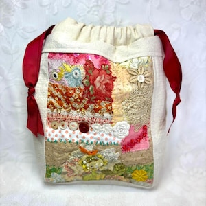 May include: A cream-colored drawstring bag with a patchwork design. The patchwork features floral patterns, lace, and various embellishments in shades of pink, orange, and green. Red ribbon ties the bag closed.