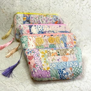 May include: Four colorful, patchwork fabric pouches with zipper closures and tassel accents. The pouches feature a variety of floral and geometric patterns in pastel colors. The tassels are in shades of gold, pink, and purple.
